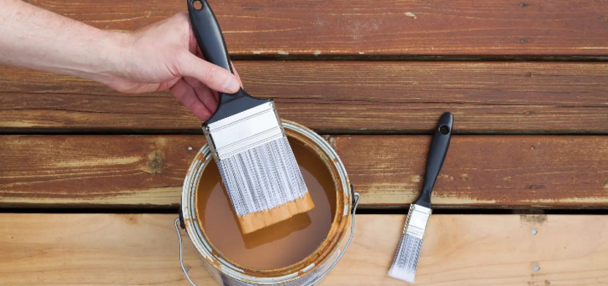 How to maintain wooden decks - hand dipping paintbrush into a can of wood stain for a fading wood on an outdoor deck